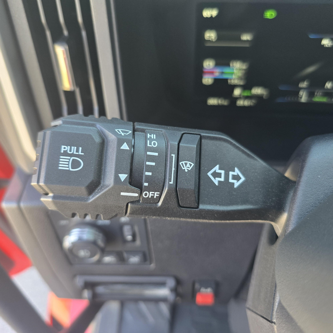 Steering column stalks and dashboard controls in a Mack PR64T76H showing turn signal lever, headlight control, and wiper switch.