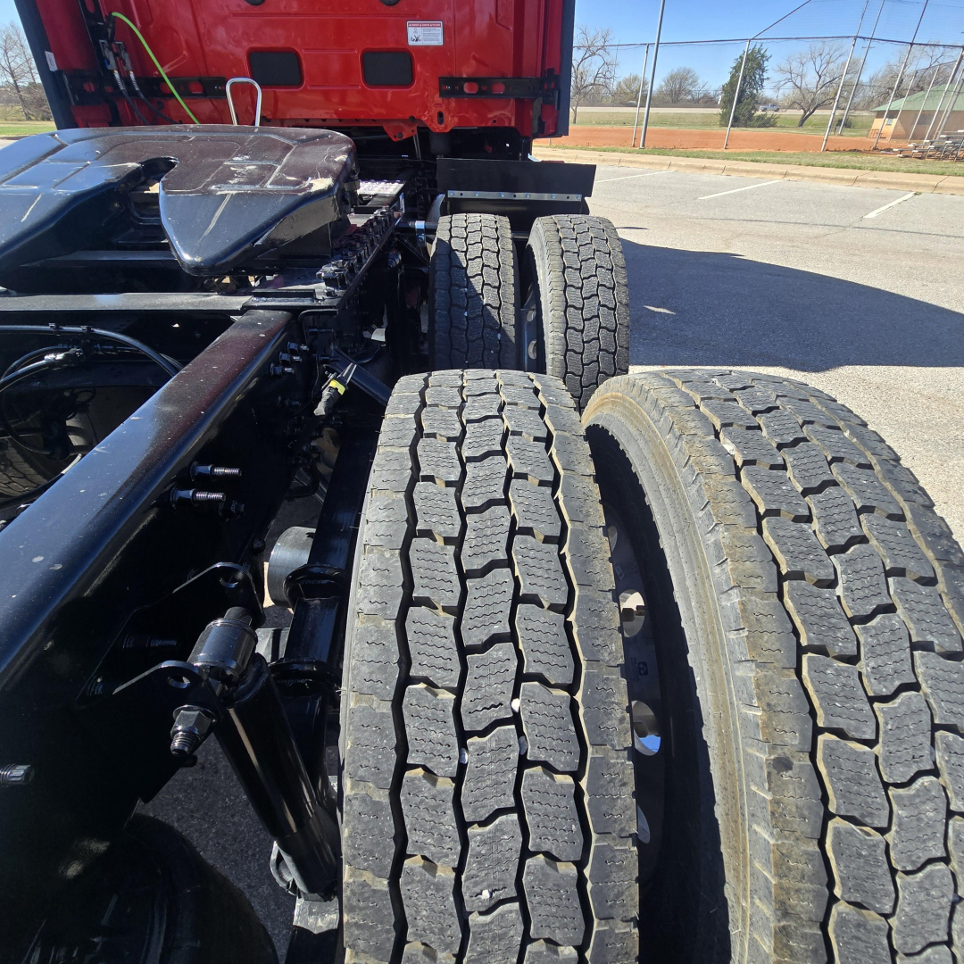 Mack PR64T76H truck chassis and dual rear axles with treaded tires visible, cab in red, engine bay area not visible.