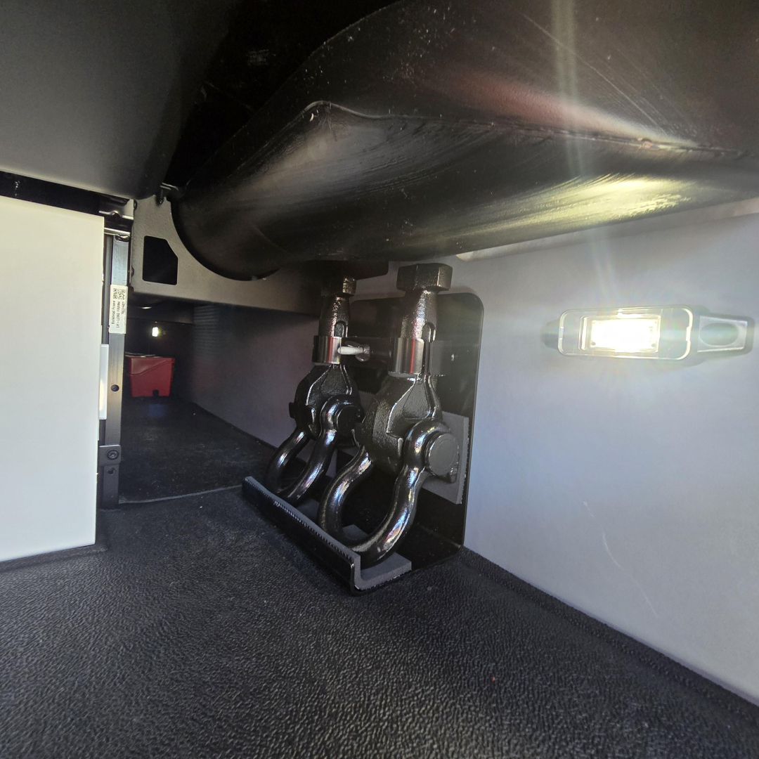 Conventional sleeper truck undercarriage showing air suspension hubs and mounting hardware with a trailer hitch area and interior side paneling.