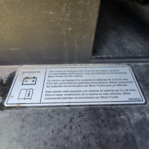 Label on Mack truck showing 12V/24V battery system and battery recommendations in English, French, and Spanish.