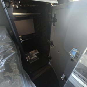 Cab interior of a new 2026 Mack PR64T76H sleeper truck showing an open side cabinet with shelves and a brochure inside; door panels and latches visible.