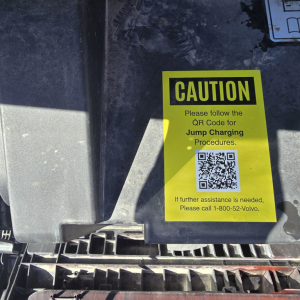Caution label on Mack truck component showing QR code for jump charging procedures.