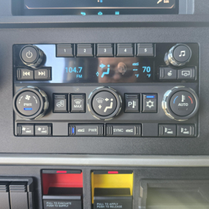 Dashboard of a 2026 Mack PR64T76H showing climate controls, radio display 104.7 FM, temperature 70°F, and various control buttons.