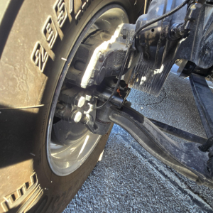 Truck front axle with tire and suspension components visible showing wheel hub and brake assembly.