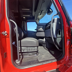Interior cabin of a red Mack truck with open door showing driver seat, steps, and dashboard view.