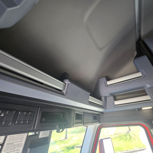 Cab interior upper dash area of a Mack PR64T76H showing overhead shelves and interior panels.