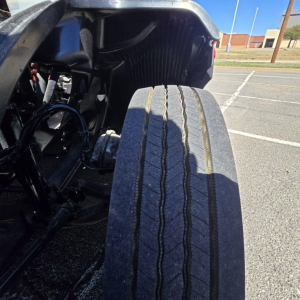Truck rear dual tires with suspension components and chassis visible in foreground; Mack PR64T76H branding not visible.