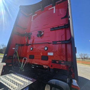 Rear view of a red Mack truck sleeper cab, vertical rear doors with hinges and latches, step platform visible, clear sky.