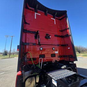 Mack PR64T76H tractor-trailer rear view showing vertical tail area, hydraulic lines, metal steps, and rear bumper with textured plate.