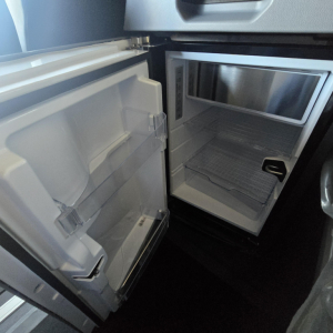 Refrigerator and compact freezer in a Mack PR64T76H truck cab showing open door compartments and interior shelves.