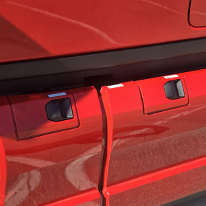 Red Mack PR64T76H truck side showing exterior storage boxes with latches and handles, glossy paint visible.