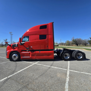 2006 Mack PR64T76H conventional sleeper truck tractor side view showing red cab and three rear axles with chrome wheels.