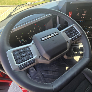 Mack steering wheel in a truck cockpit with control clusters on both sides and a digital instrument display in the dash.