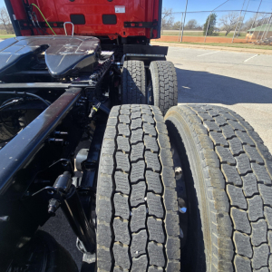 Mack PR64T76H truck chassis and dual rear axles with treaded tires visible, cab in red, engine bay area not visible.