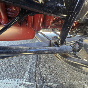 Mack PR64T76H truck undercarriage showing suspension and driveline components, including a red engine/oil pan area and black stabilizer bar.