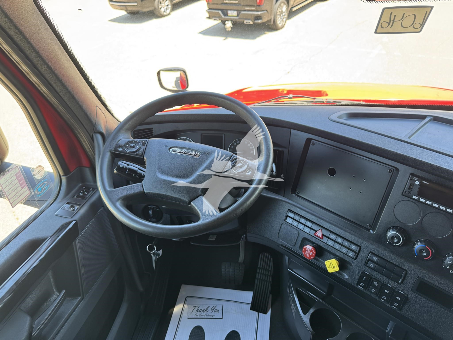 Truck cab interior showing steering wheel and dashboard of a Freightliner Cascadia, with instrument cluster, center console, and large touchscreen display.