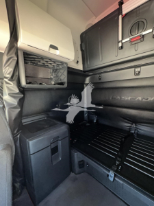 Interior cab of a 2023 Freightliner Cascadia 126 sleeper showing storage compartments and bunk area with cabinets and panels.