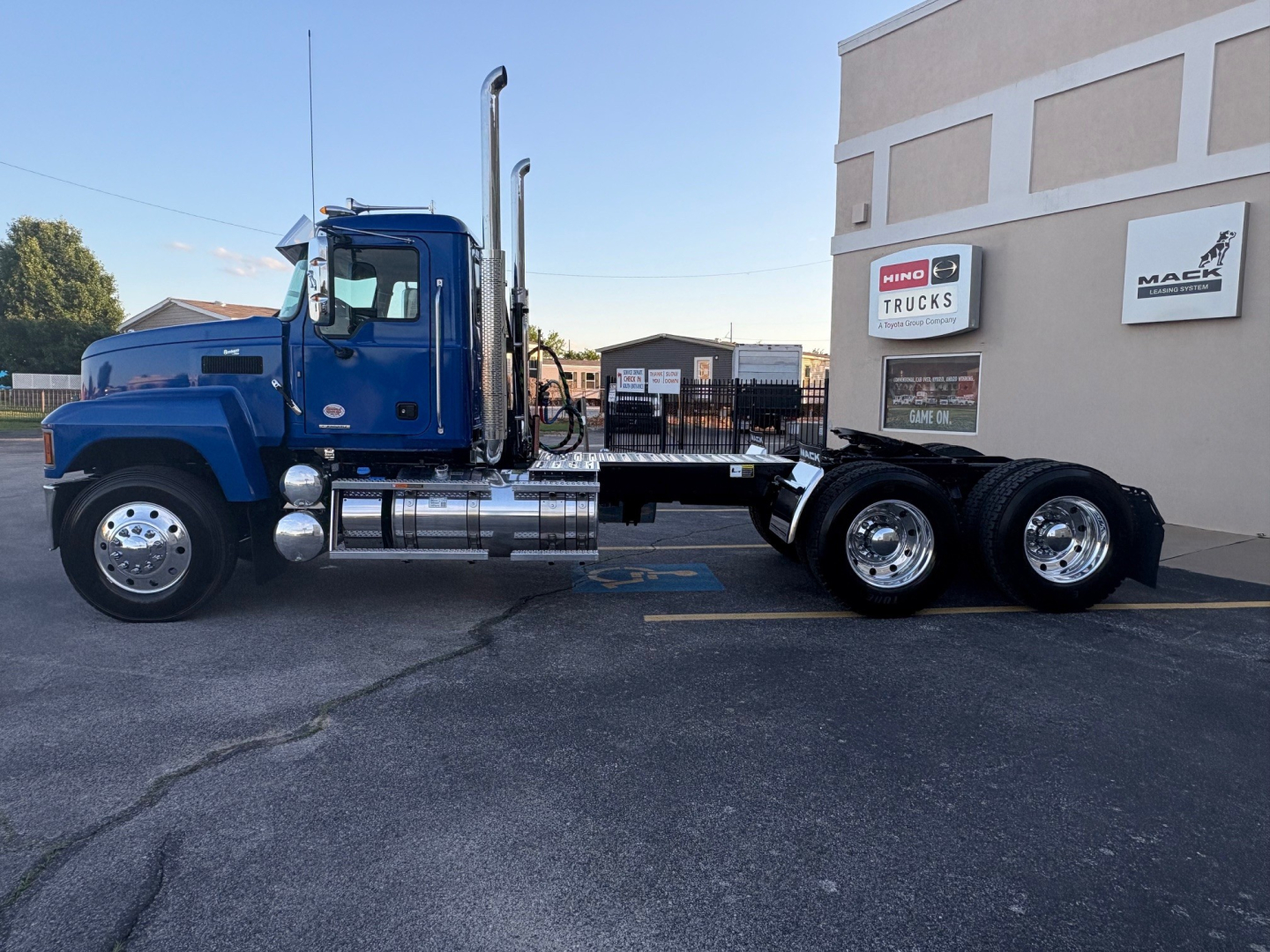 Blue 2026 Mack PI64T conventional daycab truck side view showing cab, chrome fuel tanks, and dual rear axles.