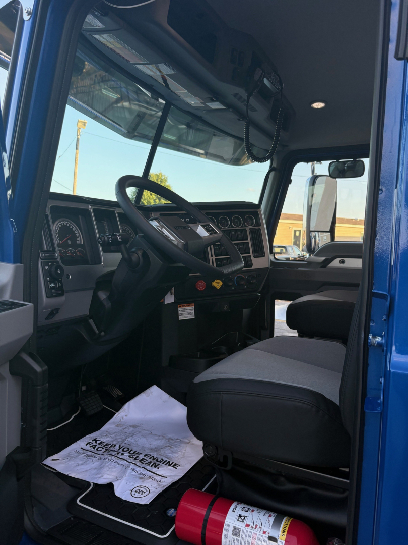 Cab interior of a 2026 Mack PI64T truck showing steering wheel, dashboard gauges, driver seat, and front passenger area; visible window, mirrors, and a floor mat.