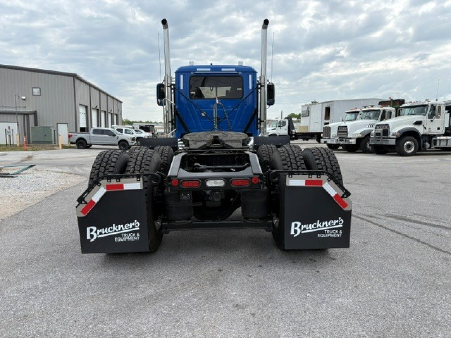 Rear view of a blue Mack PI64T tractor without a trailer, showing dual rear axles, mud flaps with Bruckner Truck Equipment logos, and twin exhaust stacks.
