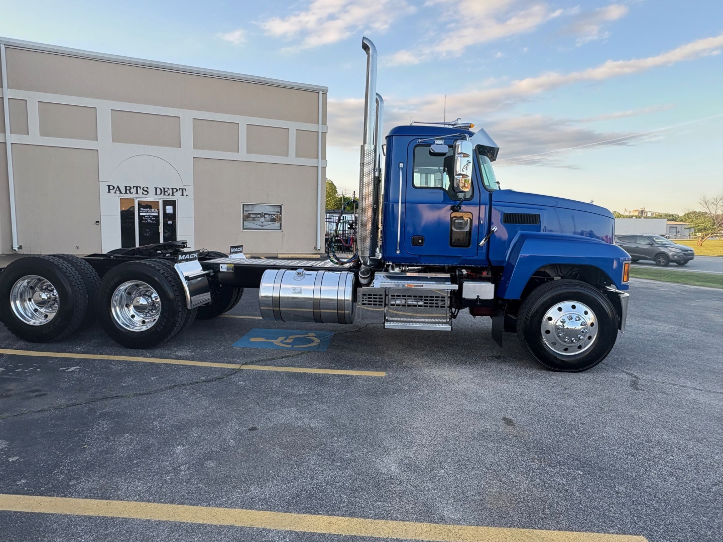 Mack PI64T truck in blue cab, side view showing cab, exhaust stack, fuel tanks, and dual rear axles in a parking lot.