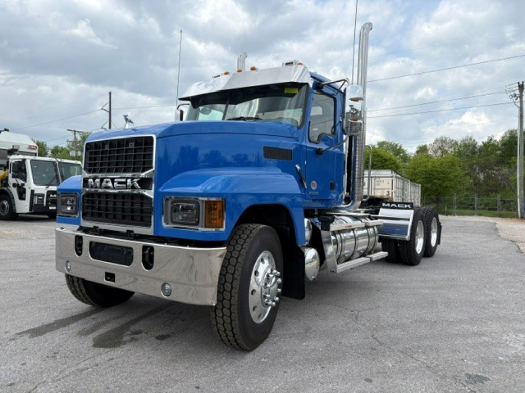 Mack PI64T conventional daycab truck in blue, front three-quarter view showing chrome bumper, grille, large exhaust stack, and dual rear axles with chrome fuel tanks.