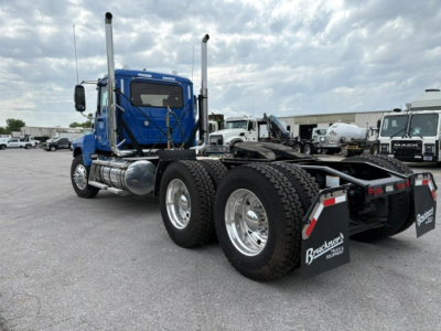 Mack PI64T truck tractor in blue, side view showing elevated exhaust stacks and dual rear axles with heavy-duty tires; Brackett mud flaps with hydraulic parking area.