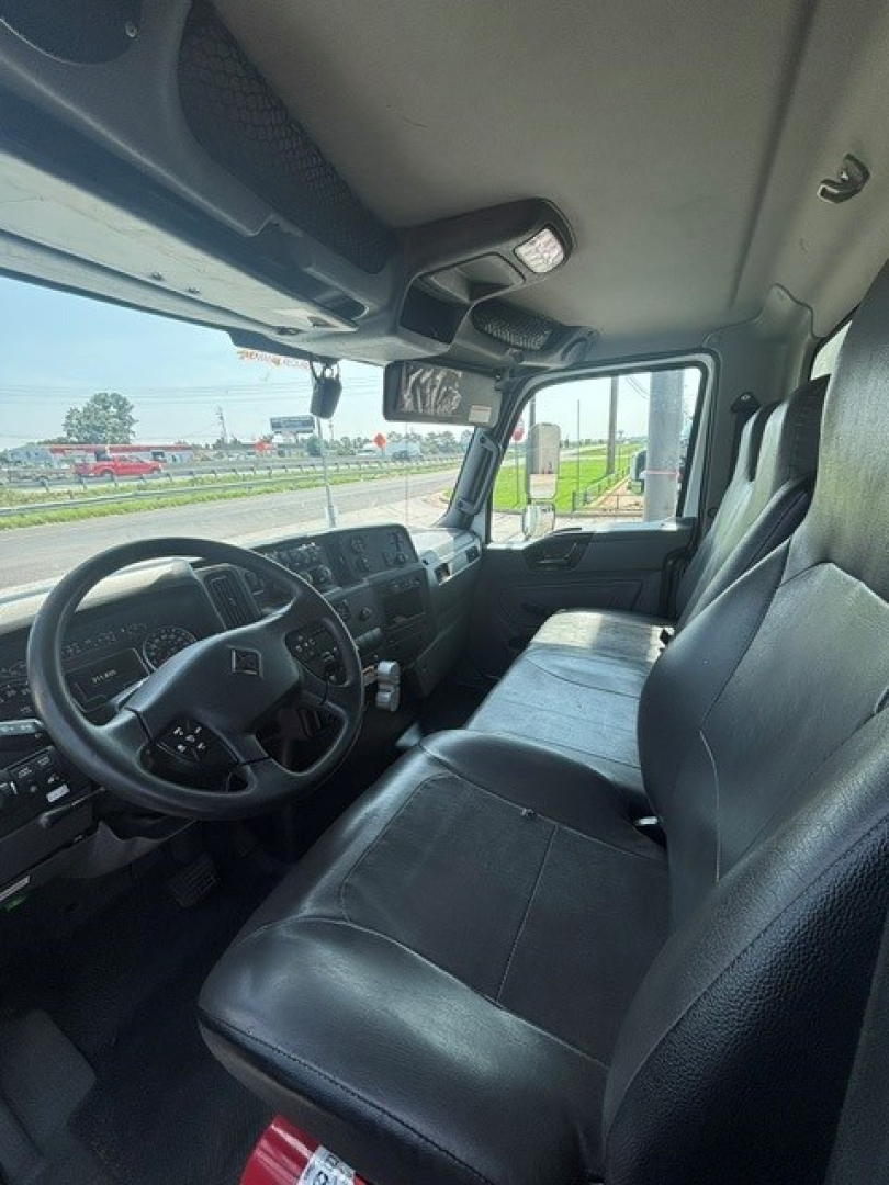Cab interior of a 2021 International MV607 truck showing steering wheel, dashboard, driver seat, and front passenger seat with a view of the windshield and side mirror.