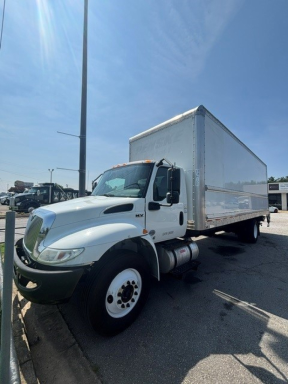 Box truck with a white cab and large silver box body in a dealership lot. The International MV logo on the door.