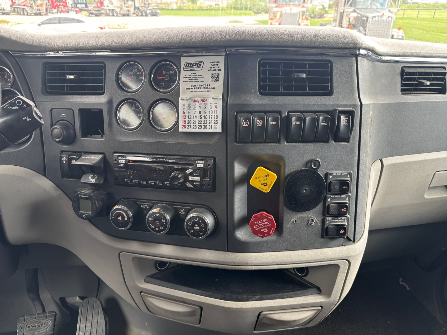 Vehicle dashboard of a 2019 Peterbilt 579 showing instrument cluster, switches, warning labels, and a calendar sticker.