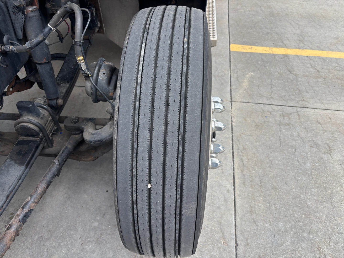 Truck wheel and suspension side showing 2019 Peterbilt 579 chassis area and front dual mount; visible tire tread with ribbed grooves.