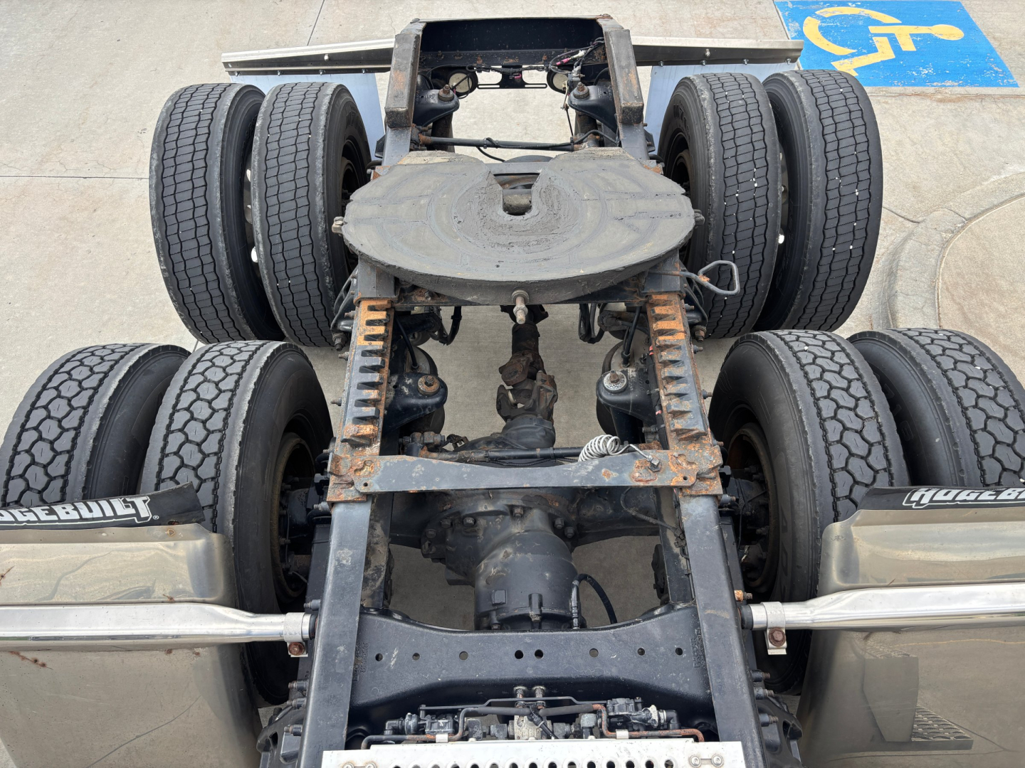 Vehicle chassis showing fifth-wheel and triple-axle rear with dual tires in view.