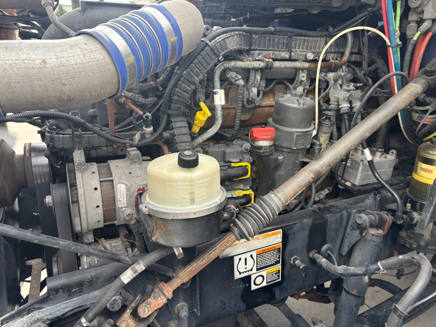 Peterbilt 579 engine bay showing air intake, coolant reservoir, hoses, wiring, and various engine components.