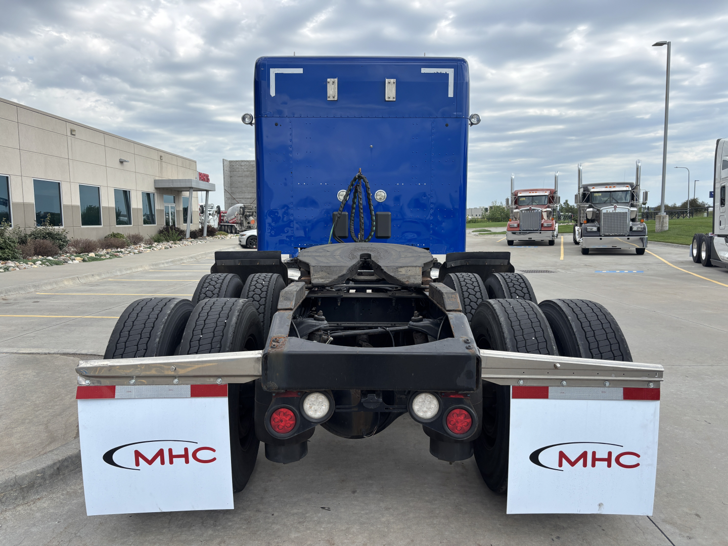 Truck chassis rear view of a 2019 Peterbilt 579, blue cab in background, dual rear axles, white MHC mudflaps, red taillights, and fifth wheel area visible.