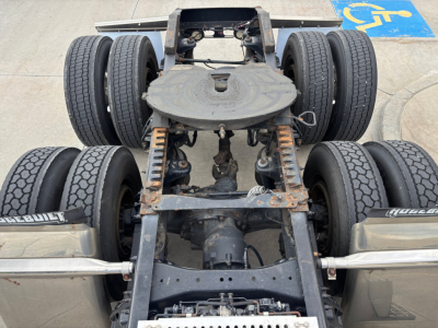 Vehicle chassis showing fifth-wheel and triple-axle rear with dual tires in view.