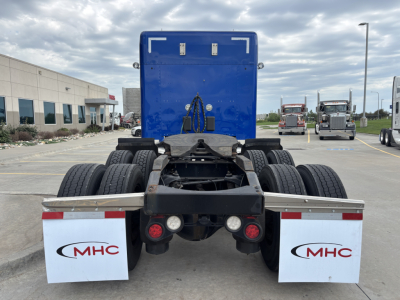 Truck chassis rear view of a 2019 Peterbilt 579, blue cab in background, dual rear axles, white MHC mudflaps, red taillights, and fifth wheel area visible.