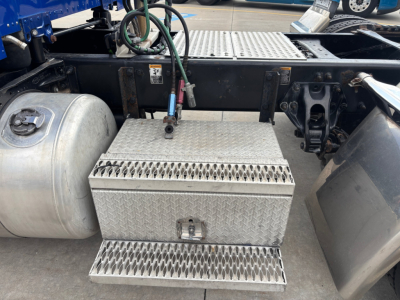 Conventional sleeper Peterbilt truck chassis showing diamond plate aluminum toolbox with ladder step, fuel tank, and wiring near the rear cab mount.