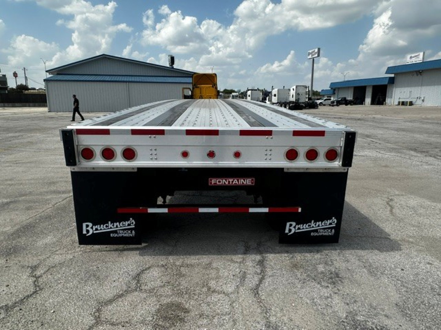 Flatbed trailer rear view showing Fontaine brand and Bruckner’s mud flaps with taillights and reflective tape.