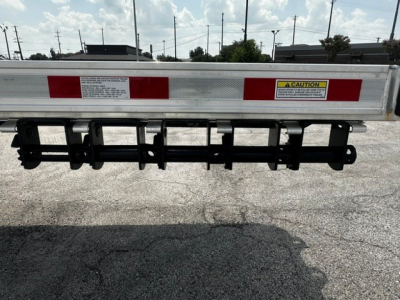Trailer rear showing reflective red/white panels and a lowered mud flap rack with warning label.