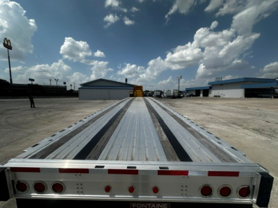 Flatbed trailer deck with metal decking and reflective tape; rear view showing taillights and rear bumper; Werner-style truck yard in background.