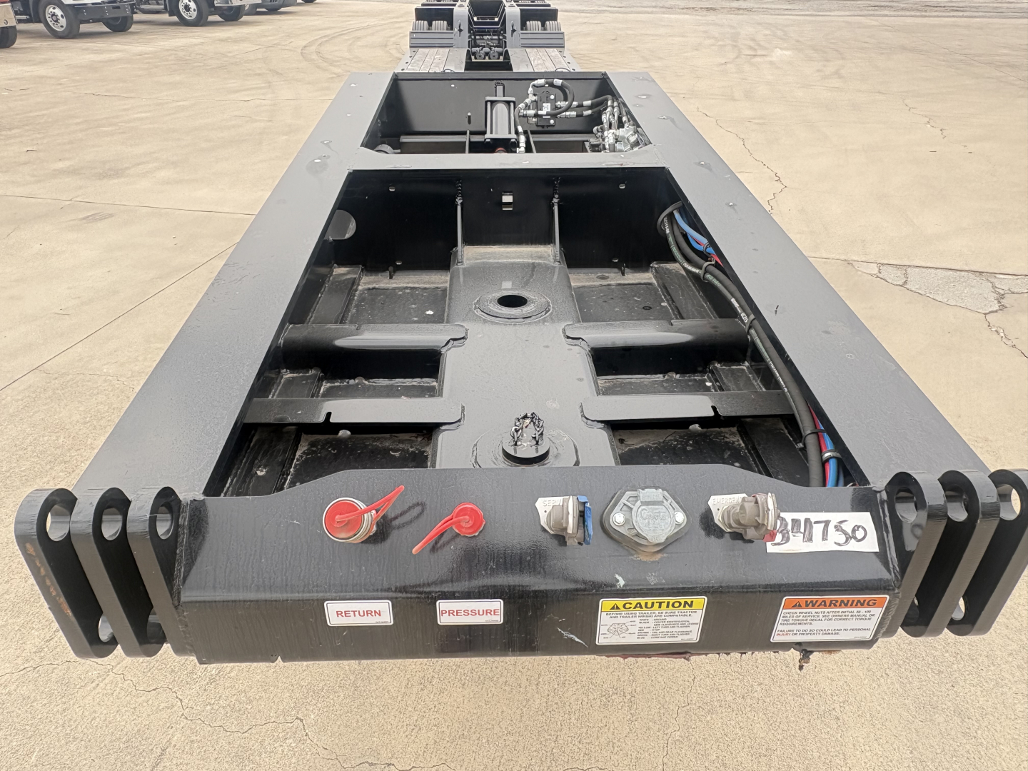Load King trailer bed, lowboy style, front view showing kingpin area and frame with hydraulic hoses, warning labels, and red safety latches.