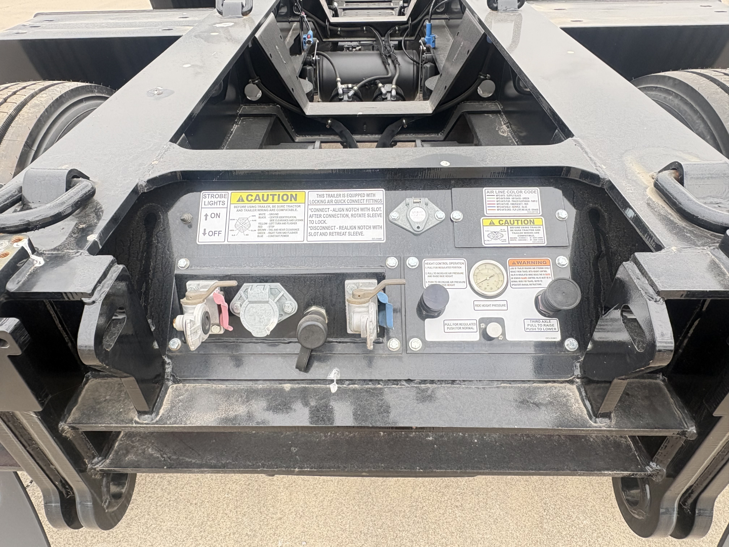 Trailer rear control panel with multiple switches, labels, and warning placards; visible are ignition-like levers, gauges, and safety labels.