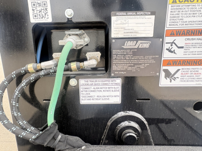 Trailer control panel area showing hydraulic hoses, green fluid line, and labels on a Load King trailer. Visible text includes FEDERAL ANNUAL INSPECTION, LOAD KING branding, and warning stickers.