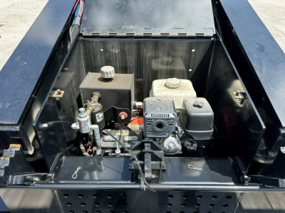 Lowboy trailer deck engine bay with hydraulic pump and control components visible, small gasoline engine, various hoses and mounting brackets.