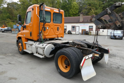 Orange Freightliner Cascadia 125 daycab semi-truck viewed from rear 3/4 with hookups and chassis, no trailer attached.