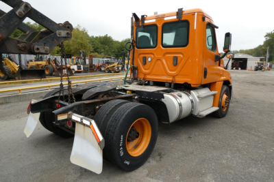 Orange Freightliner Cascadia 125 daycab rear view showing chassis and rear wheels with hitch, fuel tanks, and cab in front.
