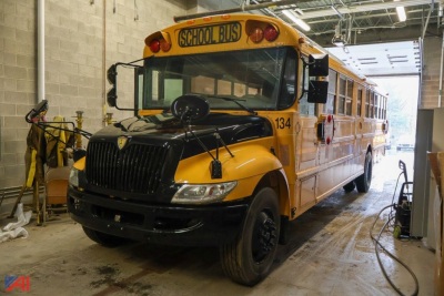 School bus in indoor lot with yellow body and black hood, front view showing 'SCHOOL BUS' sign on top, number 134 on door, and IC Corporation logo on fender.