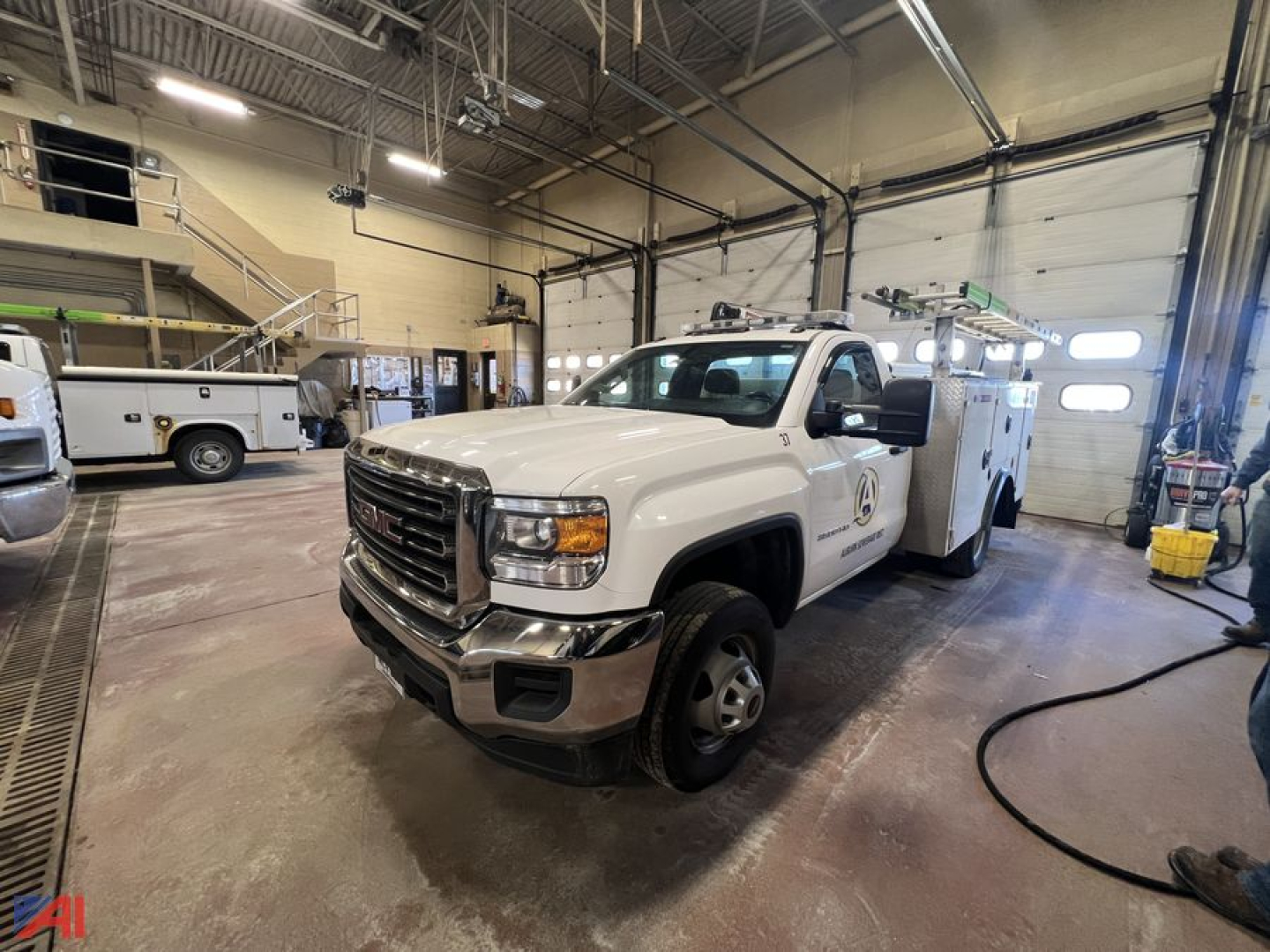 GMC Sierra 3500HD utility truck with crane in service bay, white cab, bucket truck body, front grille, headlights visible.