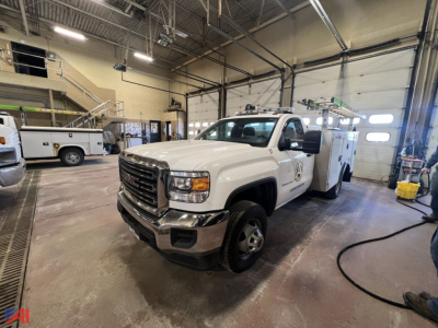 GMC Sierra 3500HD utility truck with crane in service bay, white cab, bucket truck body, front grille, headlights visible.