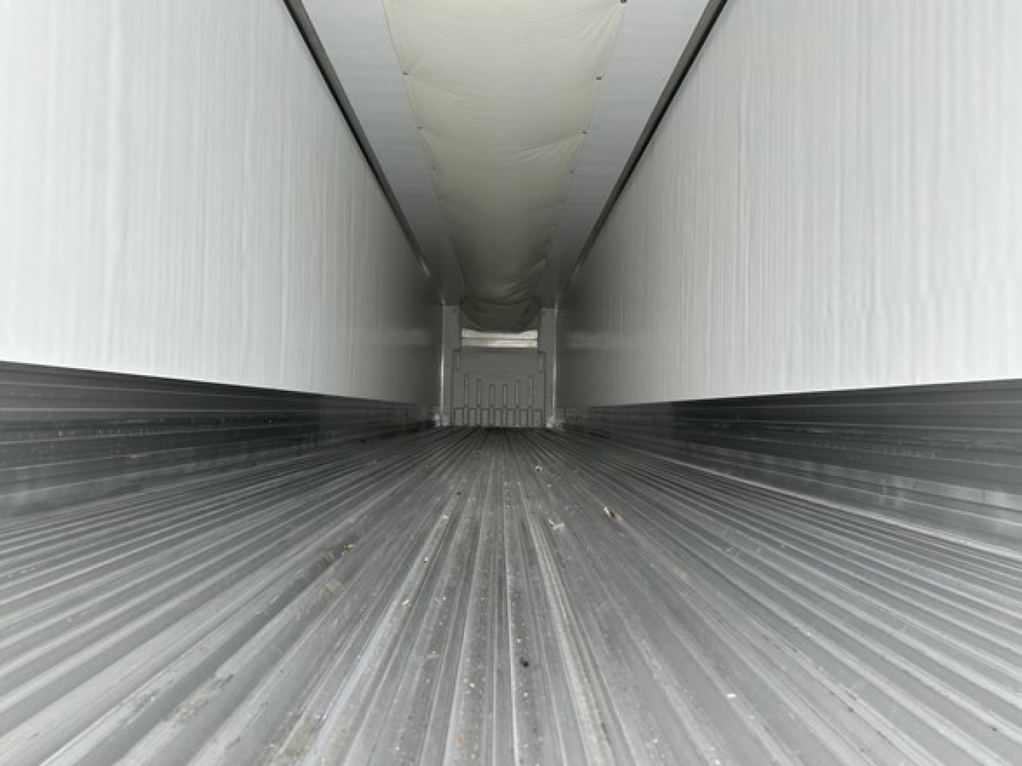 Trailer interior view into a refrigerated trailer with corrugated metal floor and insulated walls, empty cargo space, and ceiling insulation visible.